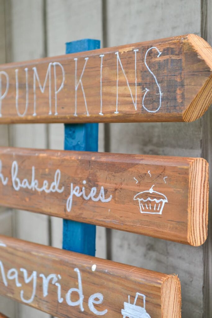 Fall front porch sign with wood arrows pointing to different fall activities like pumpkin patch, hayride, corn maze and apple picking