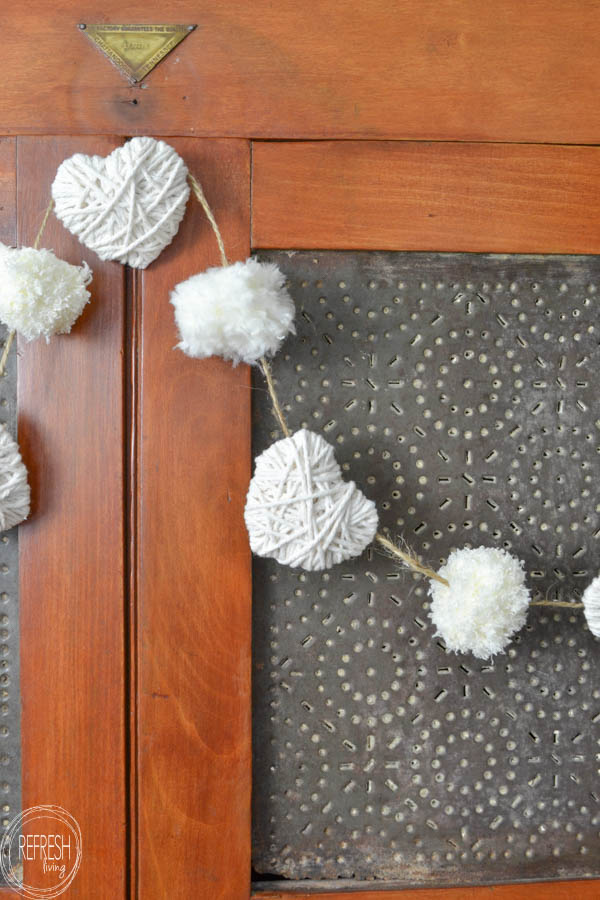 valentines garland with yarn hearts and yarn pom poms in white for neutral valentines decor