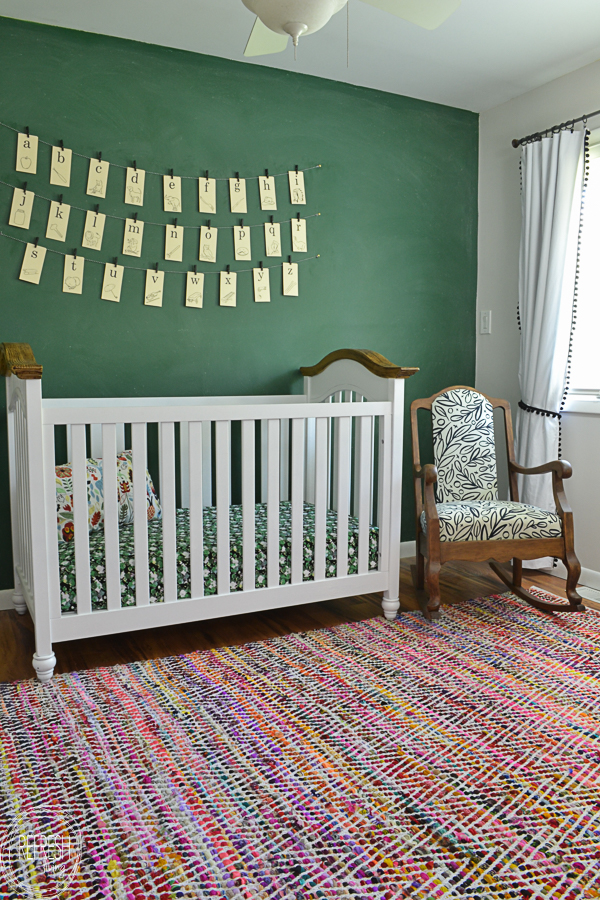 nursery with white and wood crib, colorful rug, green chalkboard wall and vintage alphabet card wall hanging