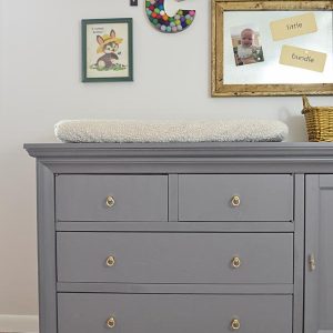 gray nursery dresser with brass pulls and used as a changing table