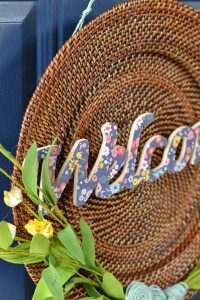 This is a plate charger - I see these at the thrift store all the time. Now, I'll definitely be picking one up to make a wreath like this one. DIY spring wreath with wood, twine, yellow flowers and welcome cut out.