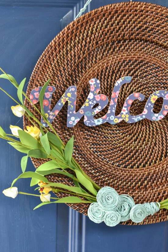 This is a plate charger - I see these at the thrift store all the time. Now, I'll definitely be picking one up to make a wreath like this one. DIY spring wreath with wood, twine, yellow flowers and welcome cut out.