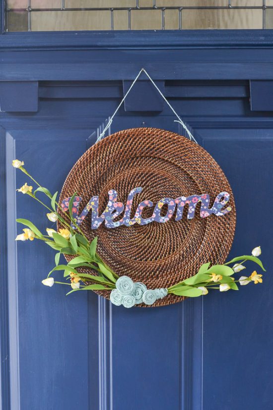 This is a plate charger - I see these at the thrift store all the time. Now, I'll definitely be picking one up to make a wreath like this one. DIY spring wreath with wood, twine, yellow flowers and welcome cut out.