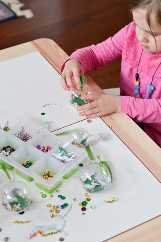 young girl filling a clear ornament to make at classroom party for Christmas with DIY ornament for kids