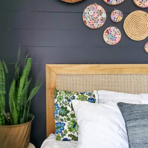 black shiplap wall in a bedroom with DIY cane headboard and vintage yo yo quilt embroidery hoop art