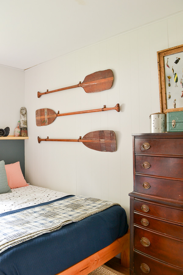 use leather hooks to solve the problem of how to hang oars on the wall. set of three vintage oars hung horizontally in  lake house bedroom 