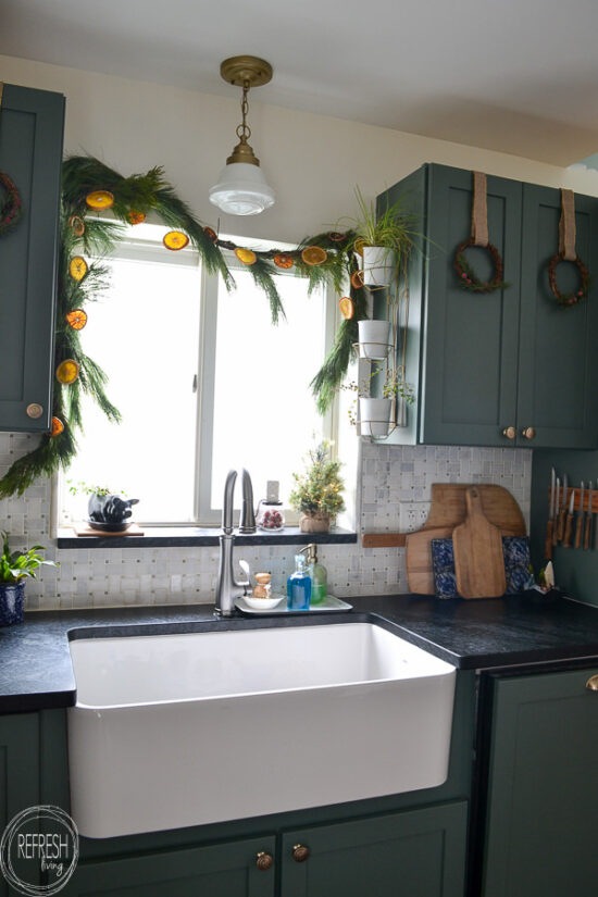 Natural wreaths and orange garland look perfect next to these green kitchen cabinets.