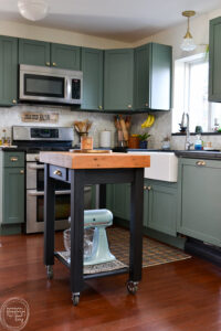 small kitchen island with butcher block top and black base in kitchen with green cabinets