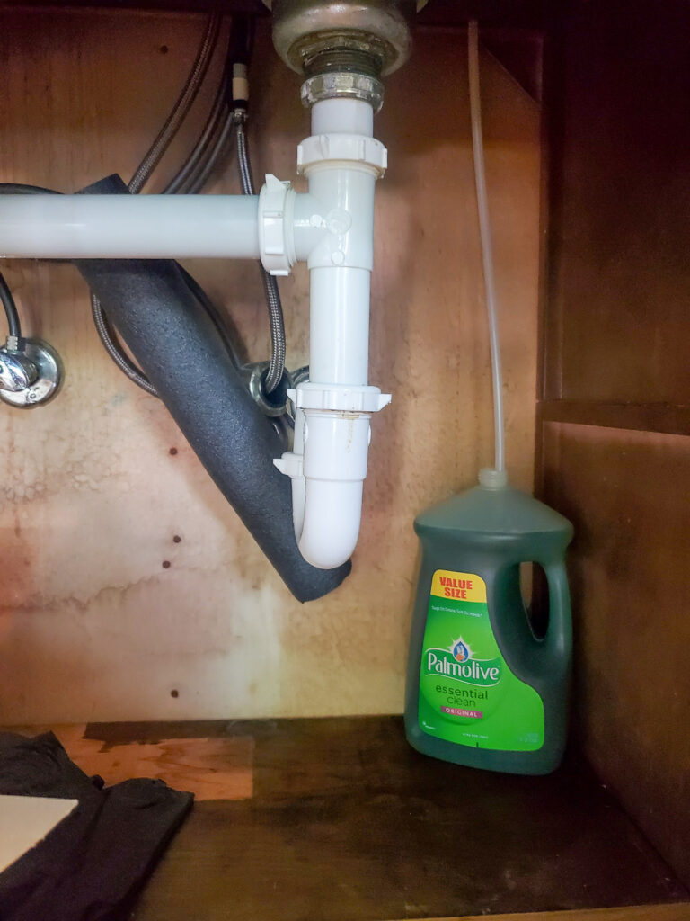 Kitchen with large bottle of dish soap under the cabinet with tube up to soap dispenser