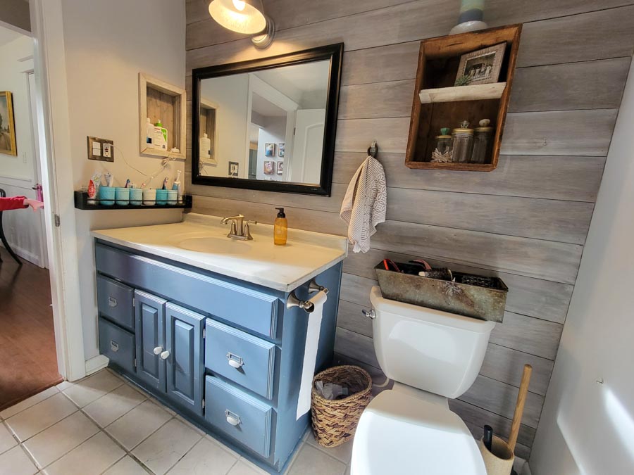 bathroom with whitewash plank wall blue vanity black mirror