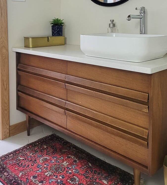 mid century modern vanity from an old dresser with marble top and top mount sink and vintage rug in bathroom